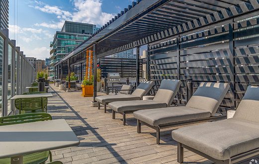 Rooftop terrace with lounge chairs, a pergola and city high-rises behind.